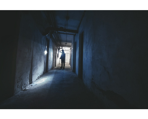 Un couloir sombre avec une personne tenant une lampe de poche pour éclairer le chemin.