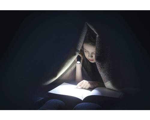Fille lisant un livre avec une lampe de poche sous une couverture