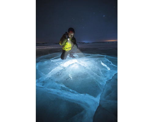 Une personne est agenouillée sur une surface de glace et éclaire la glace avec une lampe de poche.