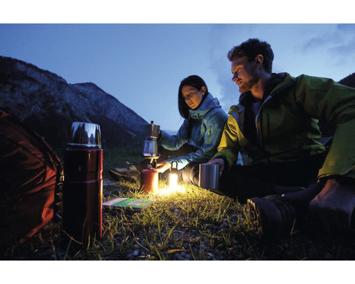 Scène de camping avec deux personnes préparant du café sur un réchaud à gaz, thermos et sac à dos au premier plan