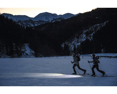 Deux personnes faisant du ski de fond de nuit avec des lampes frontales et des skis dans un paysage enneigé.