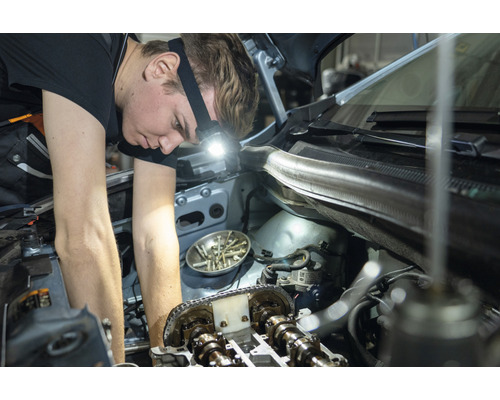 Un mécanicien répare un moteur de voiture avec une lampe frontale