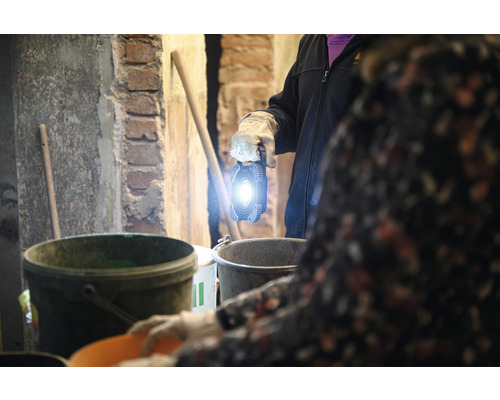 Une personne tient une lampe torche lumineuse dans une pièce avec des seaux et des outils.