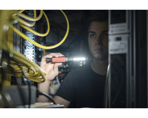 Un homme inspecte un rack serveur avec des câbles jaunes à l''aide d''une lampe de poche