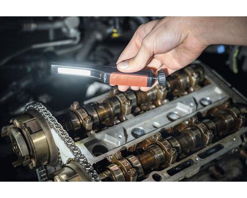 Une personne inspecte un bloc moteur avec une lampe de poche.