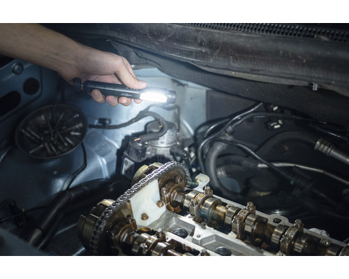 Eine Hand hält eine Taschenlampe über einen geöffneten Automotor zur Inspektion.