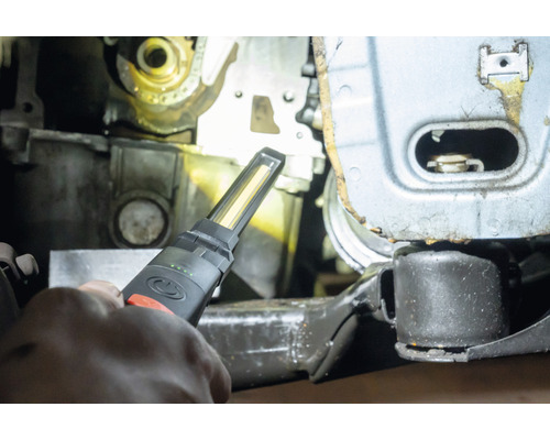 Une main tient une lampe de travail pour l''inspection des pièces de machine.