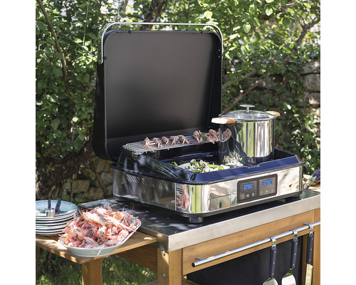 Grill extérieur multifonctionnel avec des aliments grillés, des légumes et une casserole sur une table en bois dans le jardin.