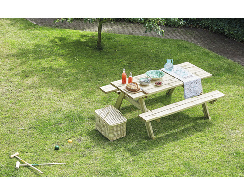 Gartenszene mit Picknicktisch aus Holz, beladen mit Geschirr, Getränken und Speisen auf einer grünen Rasenfläche.