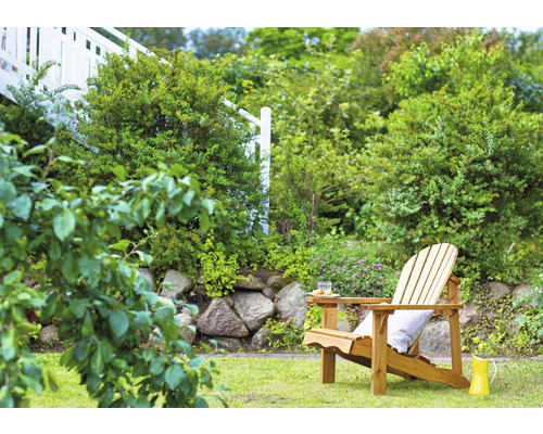 Chaise longue en bois dans le jardin sur la pelouse avec des plantes et un mur de pierre