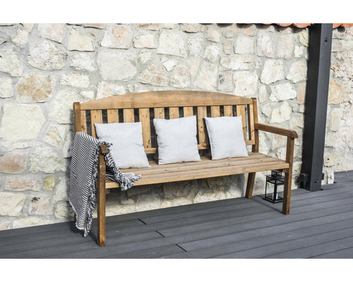 Holzbank mit Kissen und Decke vor Steinmauer