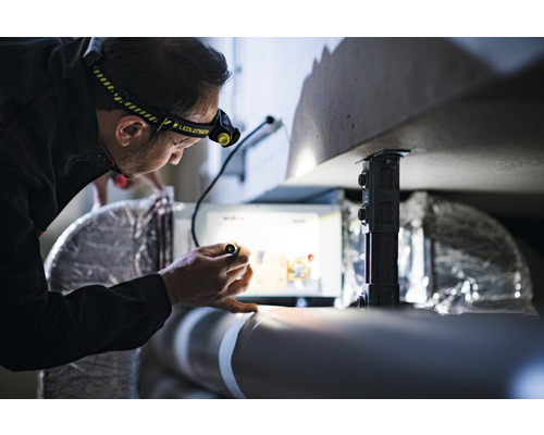 Un homme portant une lampe frontale examine des installations avec une lampe de poche.