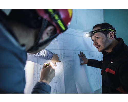 Deux ouvriers du bâtiment avec des lampes frontales regardent un plan de construction.