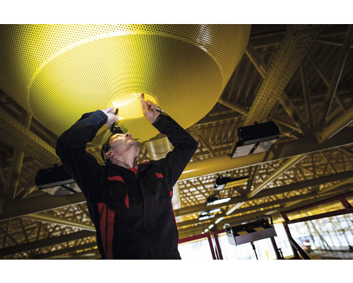 Un installateur installe un plafonnier perforé.