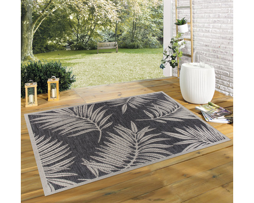 Gartenszene mit einem rechteckigen Outdoorteppich mit Pflanzenmuster auf einer Holzterrasse