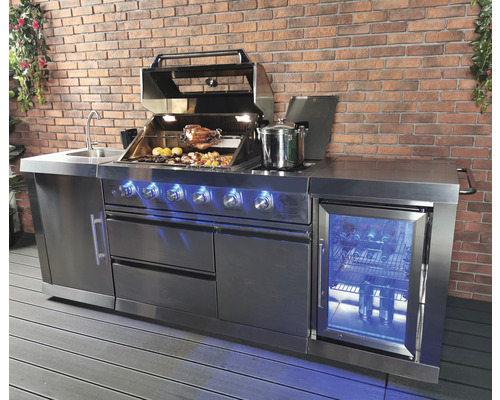 Cuisine extérieure en acier inoxydable avec barbecue, évier et réfrigérateur devant un mur de briques