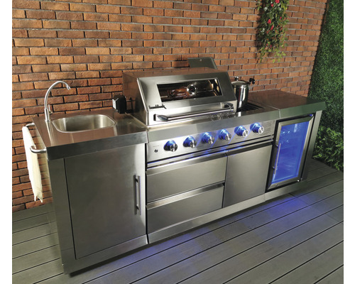 Cuisine d''extérieur en acier inoxydable avec évier, barbecue, réfrigérateur et espace de rangement devant un mur en briques.