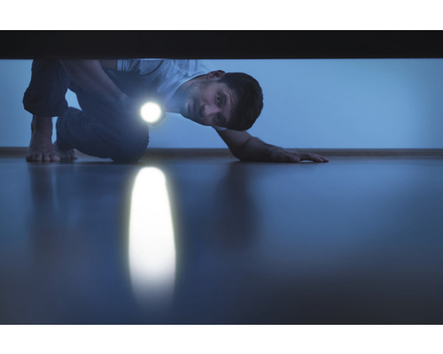 Un homme cherche avec une lampe de poche sous un meuble