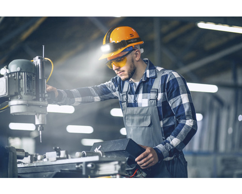 Ouvrier avec casque de protection et lampe frontale sur une machine industrielle