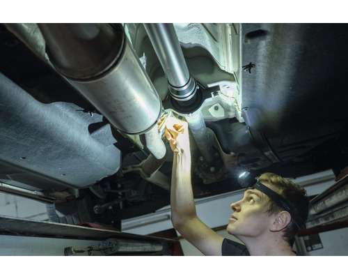 Un mécanicien inspecte un véhicule sur un pont élévateur et examine l''arbre de transmission.