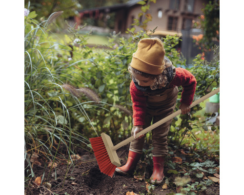 Un enfant balaie les feuilles mortes dans le jardin avec un balai de voirie.