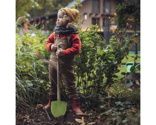 Un enfant avec une pelle se tient dans le jardin.