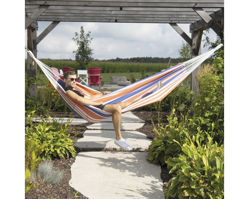 Un homme se repose dans un hamac rayé dans le jardin, sous une structure en bois.