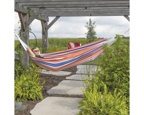 Un homme se détend dans un hamac rayé dans le jardin.