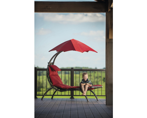 Garçon assis sur une chaise longue rouge avec parasol sur une terrasse