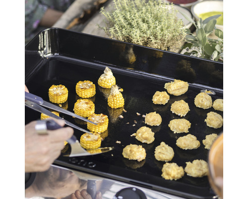 Des morceaux d''épis de maïs et des boulettes de pâte sont préparés sur une plaque de cuisson, une pince à griller est prête.