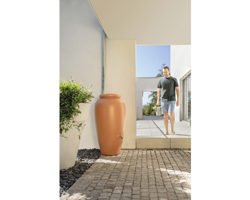 Récupérateur d''eau de pluie en forme d''amphore avec robinet à l''extérieur devant la maison