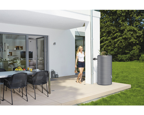 Regenwassertank aus Kunststoff neben einem Fallrohr an einem modernen Haus mit Terrasse.