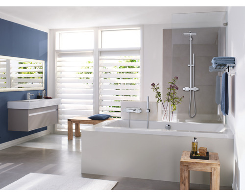 Salle de bains avec baignoire, lavabo, miroir et fenêtres à stores pour une ambiance lumineuse.