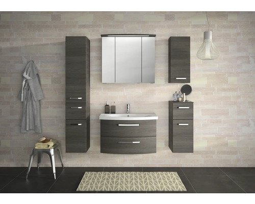 Badezimmer mit Waschtisch, Spiegelschrank und Hochschränken in Holzoptik vor einer hellen Backsteinwand.