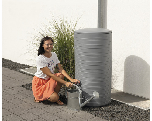 Frau mit Giesskanne und grauer Regentonne im Garten
