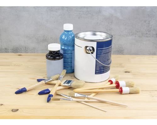 Seau de peinture, flacon de vernis et pinceaux sur une table en bois