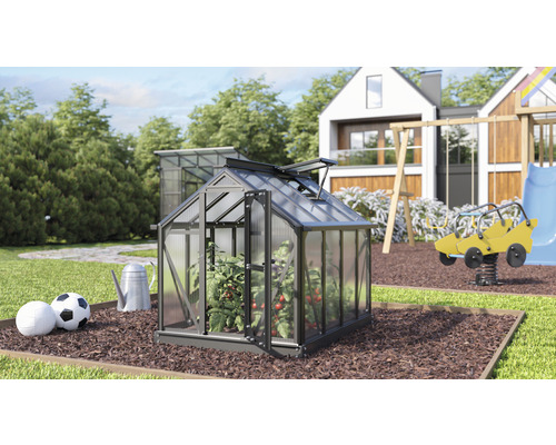 Gartenszene mit Gewächshaus, Spielplatz und Wohnhaus im Hintergrund.