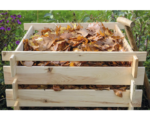 Composteur en bois rempli de feuilles et d''une bêche dans le jardin.