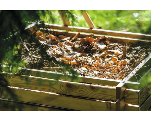 Composteur en bois rempli de feuilles et de branches dans le jardin.