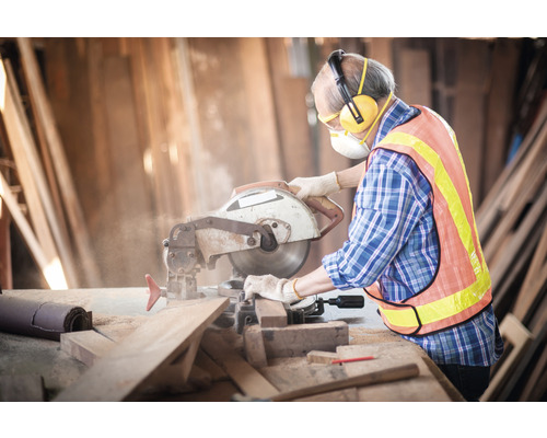Artisan utilisant une scie circulaire pour couper du bois avec un équipement de protection individuelle dans un atelier.