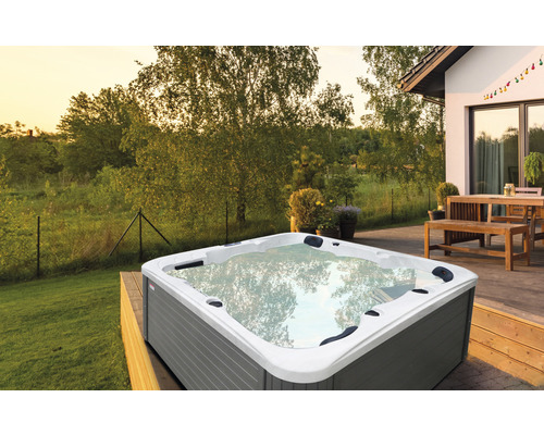 Outdoor Whirlpool auf einer Holzterrasse vor einem Wohnhaus und Bäumen