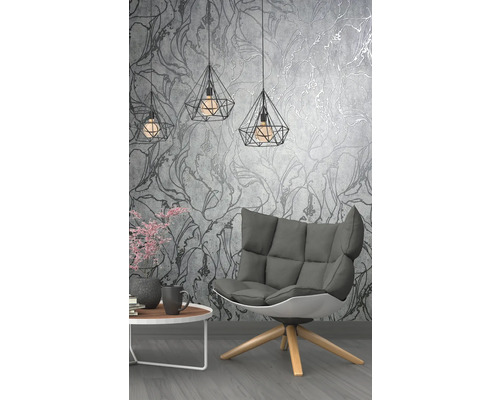 Salon avec fauteuil, table et suspensions géométriques devant un papier peint à motifs floraux