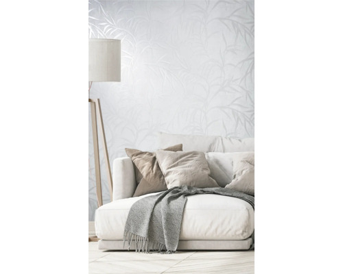 Salon avec canapé, coussins, couverture, lampadaire et papier peint à motif végétal