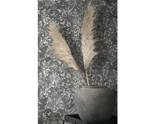 Plumes décoratives dans un vase en faïence devant un papier peint à motifs
