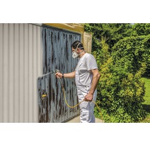 Un homme peint une porte de garage avec un pulvérisateur de peinture. Bricolage dans le jardin.
