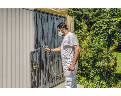 Un homme peint une porte de garage avec un pulvérisateur de peinture. Bricolage dans le jardin.