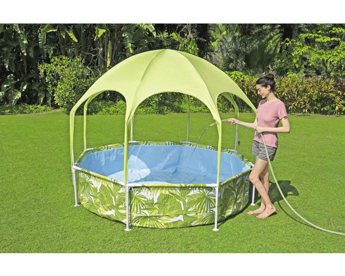 Gartenszene mit einem Framepool mit Blättermuster und Sonnenschutzdach, während eine Frau den Pool mit einem Gartenschlauch befüllt.