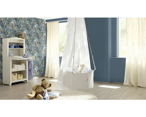 Ein helles Kinderzimmer mit Wickelkommode, Hängekörbchen und einem Teddybär auf einem Teppich