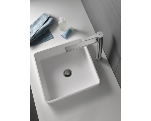 Sur un lavabo se trouvent un lavabo à poser avec robinet, une serviette et des articles de toilette