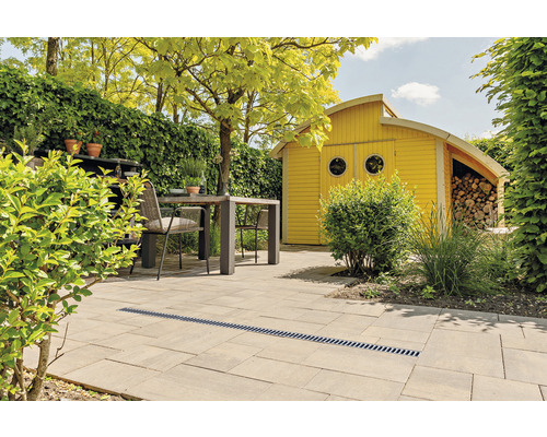 Jardin avec terrasse en pierre, caniveau de drainage, coin salon et cabanon de jardin jaune